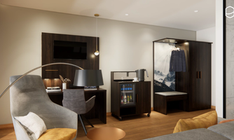 A modernly furnished hotel room with a comfortable chair, a desk, and a TV. The room has a wardrobe and a minibar.