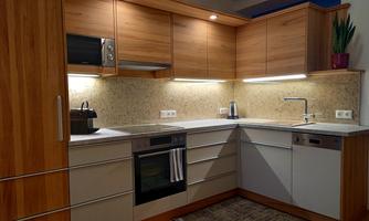 A modern kitchen with wooden cabinets and bright lighting elements. The countertop is made of a light material and there are various kitchen appliances.