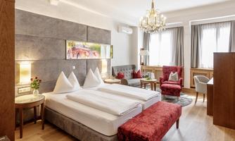 A stylish hotel room with two beds, a cozy seating area, and natural light sources. The modern furnishings and warm colors create an inviting atmosphere.