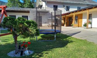 A well-maintained garden with a trampoline and a small tree. In the background, there is a house with a terrace.