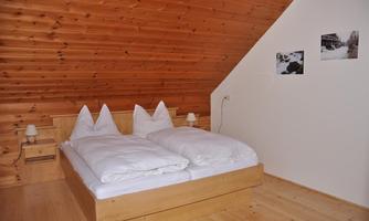 A cozy bedroom with a wooden ceiling and a double bed. The room is bright and simply furnished, perfect for a relaxed atmosphere.