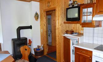 A cozy kitchen with wood paneling and a wood stove. In the background, there is a passage to another room.