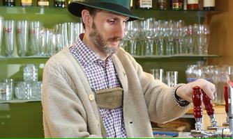 A man in traditional attire is tapping beer at a bar. In the background, glasses and a green wall are visible.