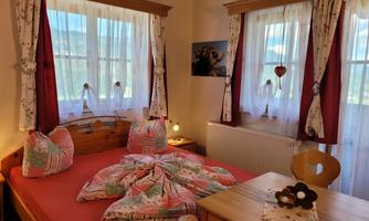 A cozy bedroom with a large bed and colorful pillows. Bright windows and wooden details give the room an inviting atmosphere.