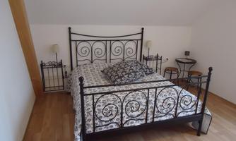 A cozy bedroom with a wrought-iron bed and floral bedding. Next to the bed are nightstands and a small table.