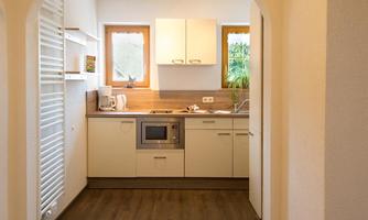A modern kitchen with bright furniture and a wooden floor. Large windows provide plenty of natural light.