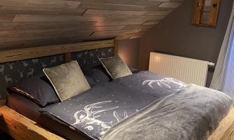 A cozy bedroom with a large wooden bed and a stylish, modern design. The walls are clad in wood, and there are cushions on the bed.