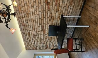 A cozy study with a table and a computer. The wall is made of brick, and a chair with a red cover stands in front of it.