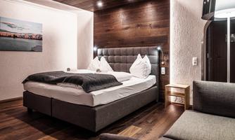 A modern bedroom with a large bed and elegant bedding. The warm wood tones and soft lighting create an inviting atmosphere.