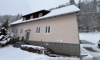 A snow-covered house in a winter landscape. The sky is gray and the surroundings feel calm and peaceful.