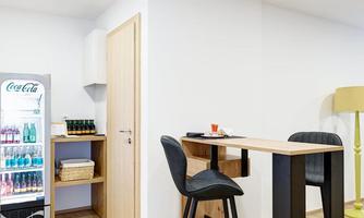 A modern room with a tall table and chairs. In the background, there is a refrigerator with drinks.