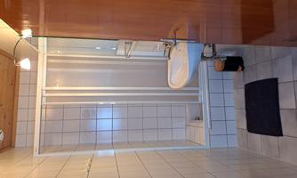 A small bathroom with a shower and a sink. The walls are tiled and the floor is equipped with tiles.