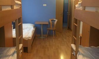 A simple room with two bunk beds and a table with a chair. The walls are blue and the floors are made of wood.