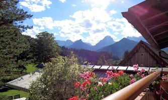 A beautiful view of the mountains under a clear blue sky. In the foreground, colorful flowers are blooming on the balcony.