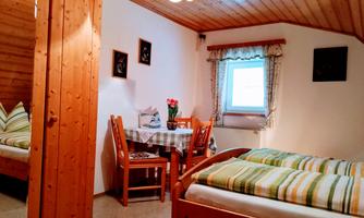A cozy room with two beds and a table. The walls are made of wood and there are windows with curtains.