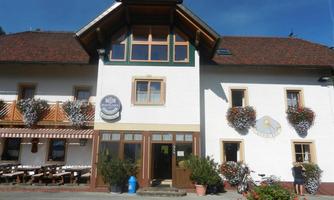 A cozy inn with a bright building and wooden cladding. Flowers hang from the windows and there are outdoor seating areas.