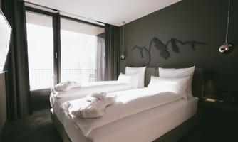 A modern bedroom with two single beds and elegant bedding. Large windows provide plenty of daylight and a view outside.