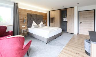 A modern bedroom with a double bed and wood paneling. Red armchairs and a light carpet give the room a cozy atmosphere.
