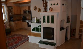 A cozy kitchen with wooden cabinets and a modern stove. The snug fireplace with green tiles creates a warm atmosphere.