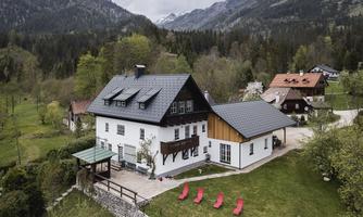 A charming mountain cabin surrounded by green meadows and mountains. In the foreground, there are red loungers on the terrace.
