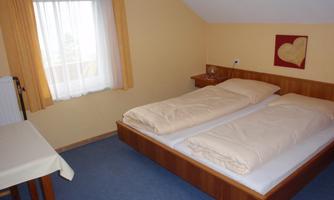 A cozy bedroom with a double bed and light bedding. The walls are in soft colors, and there is a window with curtains.