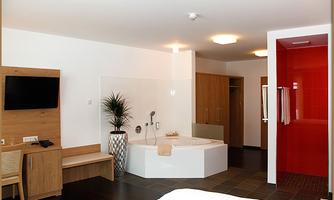 A modern room with a whirlpool bathtub and elegant furnishings. The walls are painted in warm tones, and there is a television as well as a wooden chair.