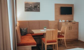 A cozy dining area with a wooden bench and chairs in warm colors. A picture hangs on the wall and a television is mounted on the wall.