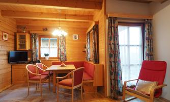 A cozy room with a wooden ceiling and wooden furniture. A dining table with chairs, a television, and large windows create an inviting atmosphere.