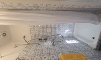 A small shower with colorful tiles and a shower curtain. Two yellow towels hang on the wall.