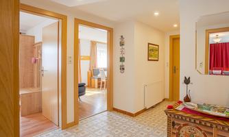A bright hallway with wooden frames and open doors to other rooms. The walls are painted light and the floor has a decorative pattern.