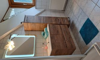 A modern bathroom with wooden cabinets and a large mirror. The window lets in plenty of daylight.