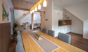 A modern dining area with a large wooden table and blue chairs. The warm lights create an inviting atmosphere.