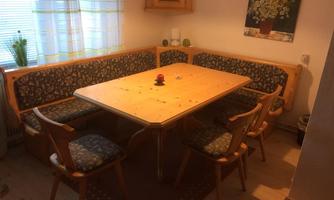 A cozy dining area with a light wooden table and upholstered benches. The room is brightly lit and has an inviting atmosphere.