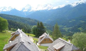 A picturesque mountain landscape with snow-capped peaks and green forests. In the foreground, cozy wooden chalets can be seen.