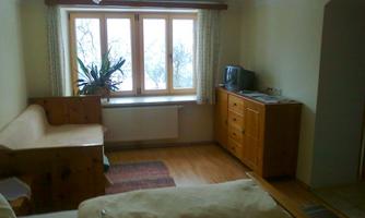 A simple room with a window, a wooden bench, and a cabinet. There is a television and a carpet on the floor.
