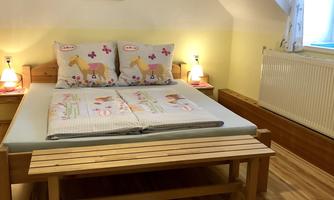 A cozy bedroom with a large bed and colorful bedcovers. There is a wooden bench and soft lighting from two bedside lamps.
