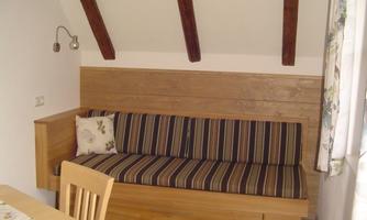A cozy room with a wooden bench and striped cushions. A wooden table stands next to it, and the walls are painted bright.