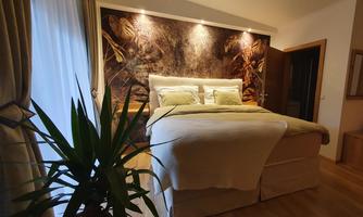 A cozy bedroom with a large bed and picturesque wall decoration. In front of the window stands a plant that creates a relaxing atmosphere.