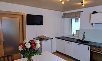 A modern kitchen with white cabinets and a bright table. On the table, there is a vase with roses and the room is well lit.