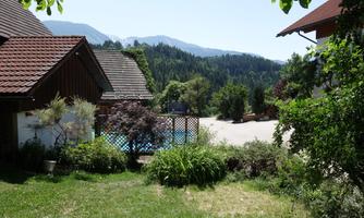 A quiet landscape with a swimming pool surrounded by trees and mountains. In the foreground, there are green meadows and bushes.