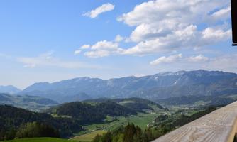 A picturesque landscape with mountains and green meadows. The sky is blue with some white clouds.