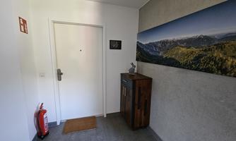 A bright hallway with a closed door and a wooden wardrobe. On the wall, there is a landscape painting.