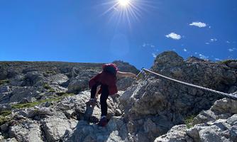 A person is climbing a rock with a rope. The sky is blue and the sun is shining brightly.
