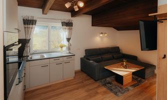 A modern living room with a cozy couch and a wooden table. The kitchen is open and well-equipped, with windows that let in a lot of light.
