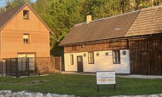 Two rustic wooden houses in a green environment. A sign provides information about the guesthouse.