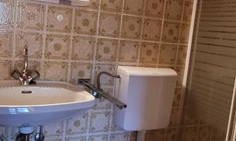 A small bathroom with a sink, toilet, and a shower. The walls are decorated with tiled patterns.