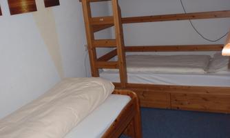 A simple bedroom with a bunk bed and a single bed. On the wall hang pictures of sunsets.