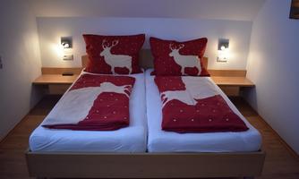 A cozy bedroom with two single beds. The bed covers and pillows are red adorned with reindeer motifs.