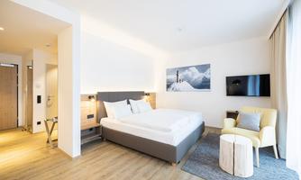 A modern hotel room with a large bed and wooden floor. The decor is bright and inviting, with a television and a cozy chair.
