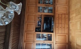 A cozy living room with a wooden cabinet and a television. The cabinet contains dishes and has glass doors.